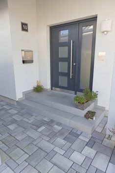 the front entrance to a modern home with steps leading up to it and plants in pots on either side