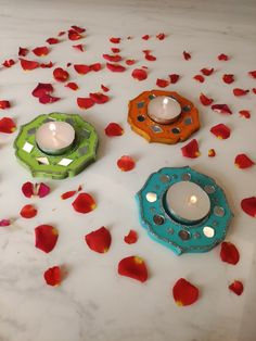 three small candles sitting on top of a table with rose petals around them and one candle in the middle