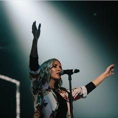 a woman holding her hand up while standing in front of a microphone on top of a stage