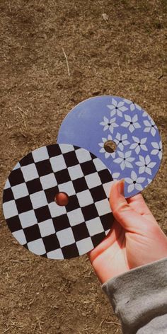 a hand is holding up two black and white checkerboard discs on the ground