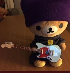 a teddy bear with a hat and guitar is sitting on a table next to a stuffed animal