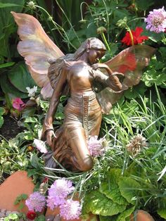 a statue of a fairy sitting in the middle of some flowers and plants with her wings outstretched