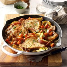 a skillet filled with potatoes and meat on top of a wooden cutting board next to plates