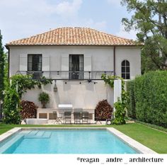 an outdoor swimming pool in front of a large house with trees and bushes surrounding it