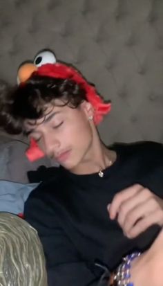 a person laying on a couch with a stuffed animal in their hair and wearing a sesame character hat