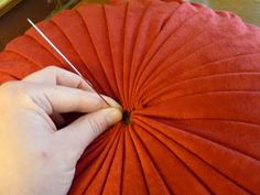 a person is sewing on an orange pillow with needles in their hand and the red fabric has been folded