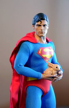 the action figure is wearing a blue and red superman suit, holding a teddy bear