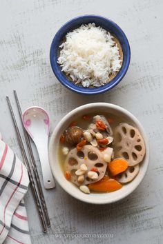 a bowl of soup with rice, carrots and other food items next to it