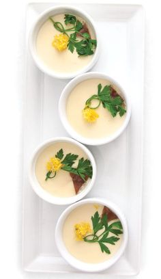 three white bowls filled with soup and garnished with green leaves