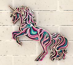 a wooden cutout of a unicorn on a white brick wall in the shape of a rainbow