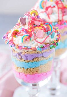 two glasses filled with rainbow colored cotton candy unicorn parfaits