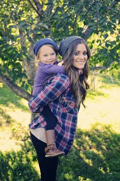 a woman holding a child in her arms while standing on the grass near some trees