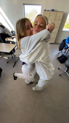 two women are hugging each other in an office setting with people sitting at desks behind them