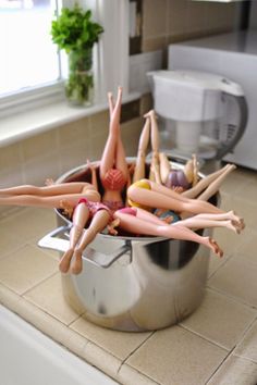 there are many dolls that are in the bowl on the kitchen counter, and one is upside down