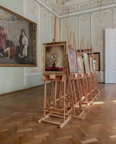 there are many paintings on easels in the middle of a room with wood flooring