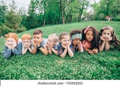 a group of children laying in the grass with their hands on their faces and smiling