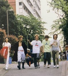 four young men walking down the street in front of some tall buildings with trees on either side