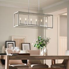 a dining room table with a vase and glasses on it, next to a light fixture hanging from the ceiling