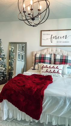 a white bed topped with a red blanket next to a christmas tree in a bedroom