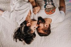 a man and woman laying on top of a bed next to each other with their heads together