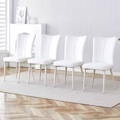 a set of four white chairs sitting on top of a wooden floor