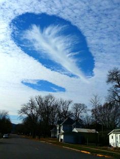 a heart shaped cloud is in the sky above two houses on a residential street with trees