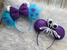 two mickey mouse ears with blue and purple hair bows on top of a white fur rug