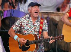 an older man singing and playing the guitar on stage with other people in the background