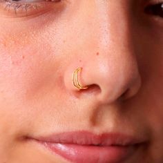 a close up of a person with a nose ring on their nose, wearing gold jewelry