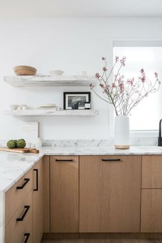 a kitchen with wooden cabinets and white marble counter tops, along with open shelving