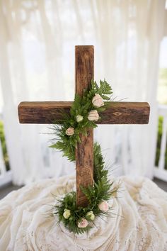 a wooden cross decorated with greenery and flowers on a white blanket in front of a window