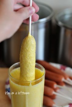 a person holding a toothpick in a glass filled with orange juice and carrots