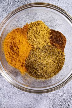 three different types of spices in a glass bowl on a gray table top, one is yellow and the other is brown