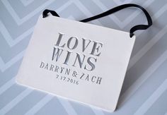 a white bag with the words love wins on it and a black ribbon hanging from it