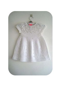 a white knitted dress hanging on a wall next to a red and white tag