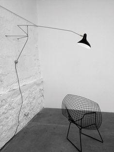 a black and white photo of a chair next to a wall with a lamp on it