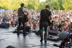 two men standing on stage with guitars in front of an audience at a music festival