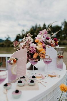 a table topped with two wine glasses filled with pink liquid and flowers on top of it