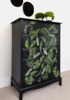 a black dresser with green leaves painted on the front and sides, along with two round mirrors above it