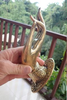 a person holding a gold statue in front of a wooden deck with trees and bushes behind it