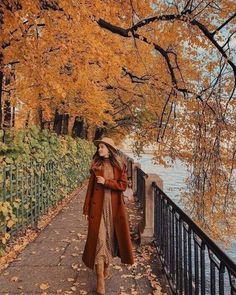 a woman walking down a path next to trees with leaves on it and the water in the background