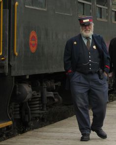 an old man in uniform walking next to a train