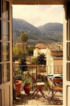 an open door leading to a balcony with mountains in the backgrouund and table and chairs