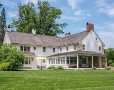 a large white house sitting in the middle of a lush green field on a sunny day