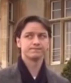 a man is standing in front of a building and looking at the camera with an indifferent look on his face