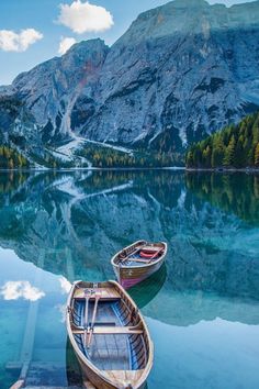 two boats are docked at the edge of a mountain lake