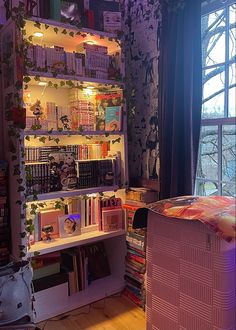 a bookshelf filled with lots of books in front of a window next to a bed