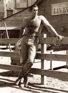 an old photo of a man leaning on a fence