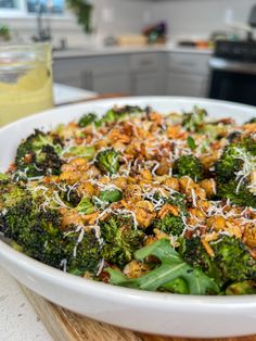 a bowl filled with broccoli and cheese on top of a wooden cutting board