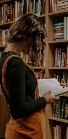 a woman standing in front of a bookshelf holding an open book